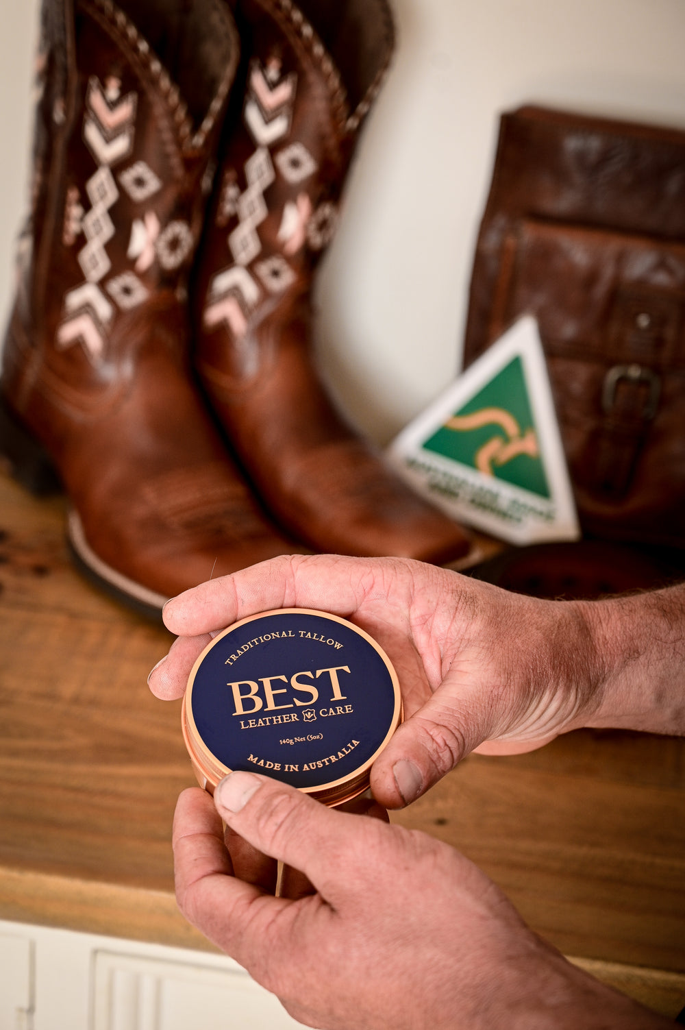 A tin of BEST Leather Care in hand, with leather boots and the Australian Made logo